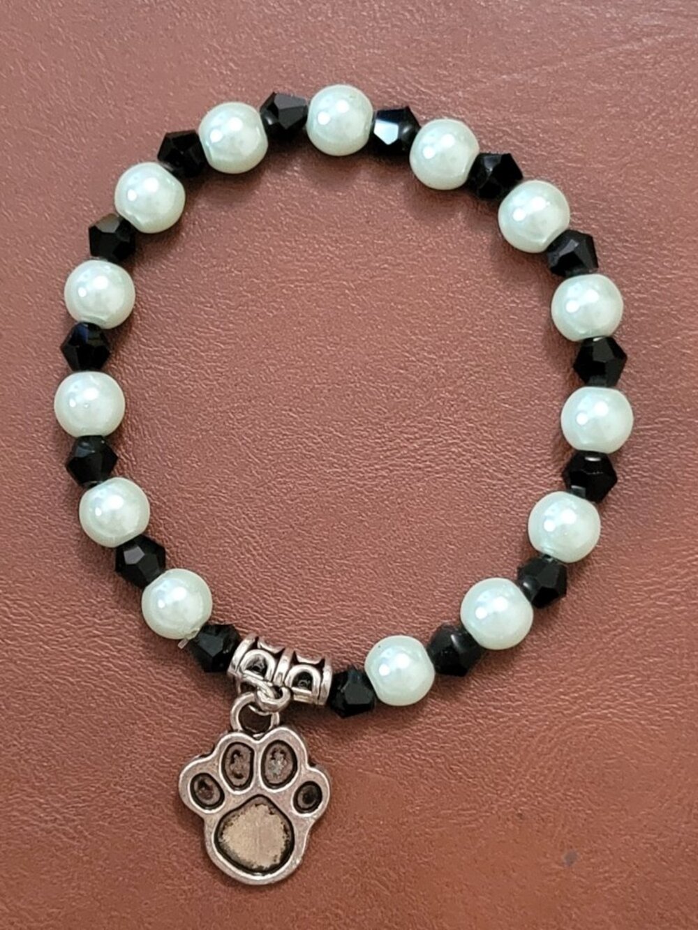 A Silver and Black Puppy Paw Charm hangs from a Black and White Wrist Wrap